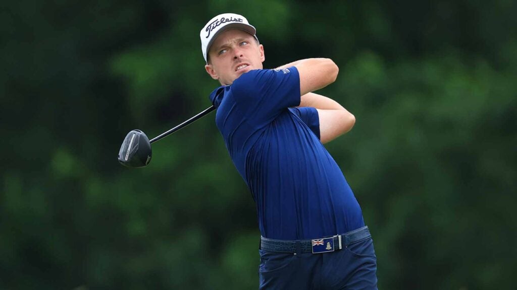 justin hastings swings driver at the u.s. open in a blue shirt and white hat