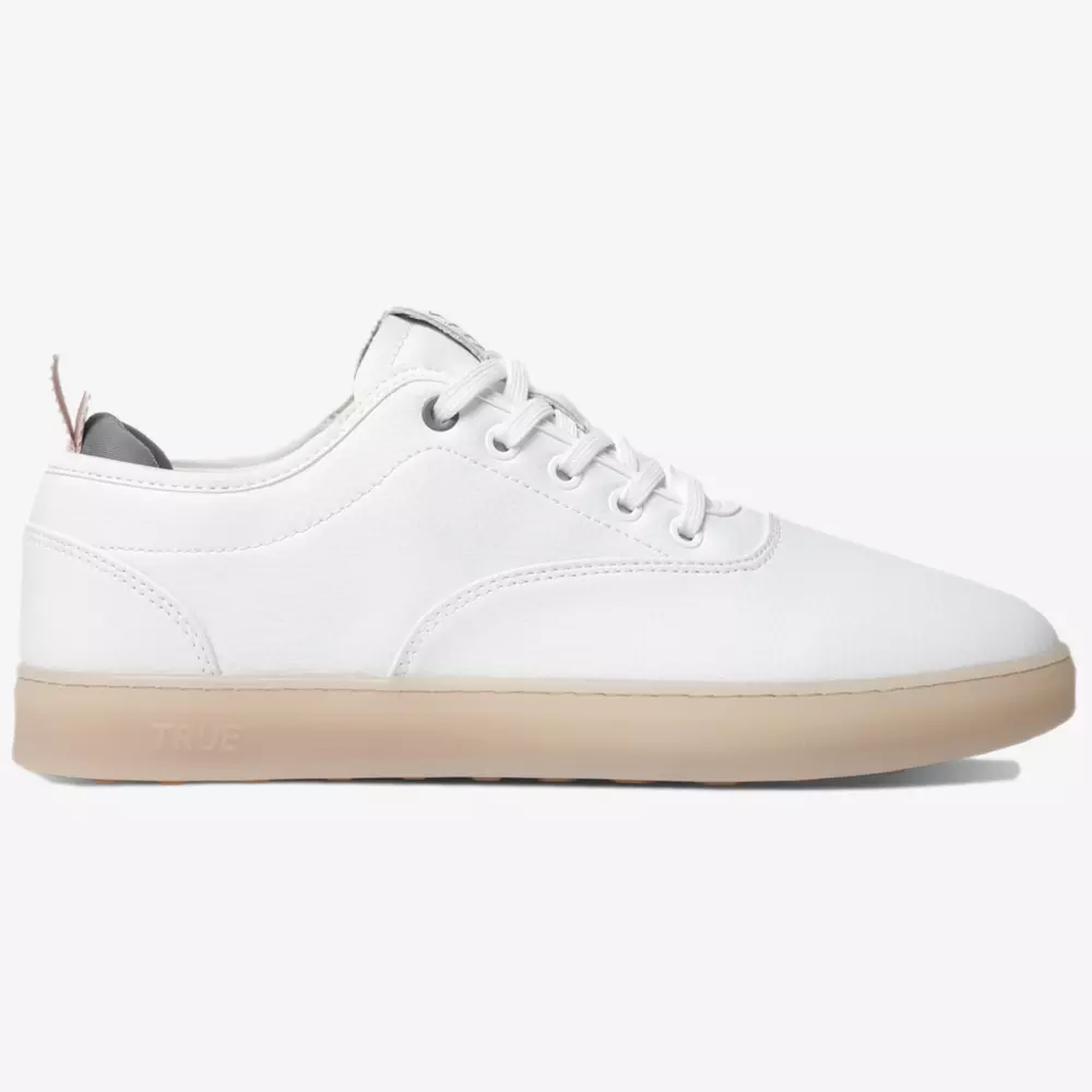 A white low-top sneaker inspired by the best women's golf shoes 2026, featuring white laces, a light tan rubber sole, minimal stitching, and a small pull tab at the heel, displayed on a plain white background.