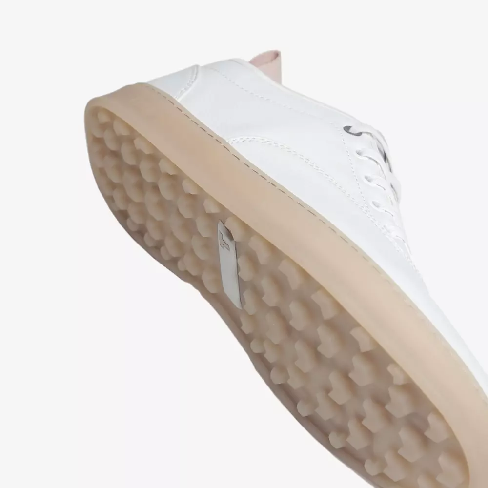 A close-up of a white sneaker, inspired by the best women's golf shoes 2026, held at an angle to highlight its textured, beige rubber sole with raised circular patterns against a plain white background.