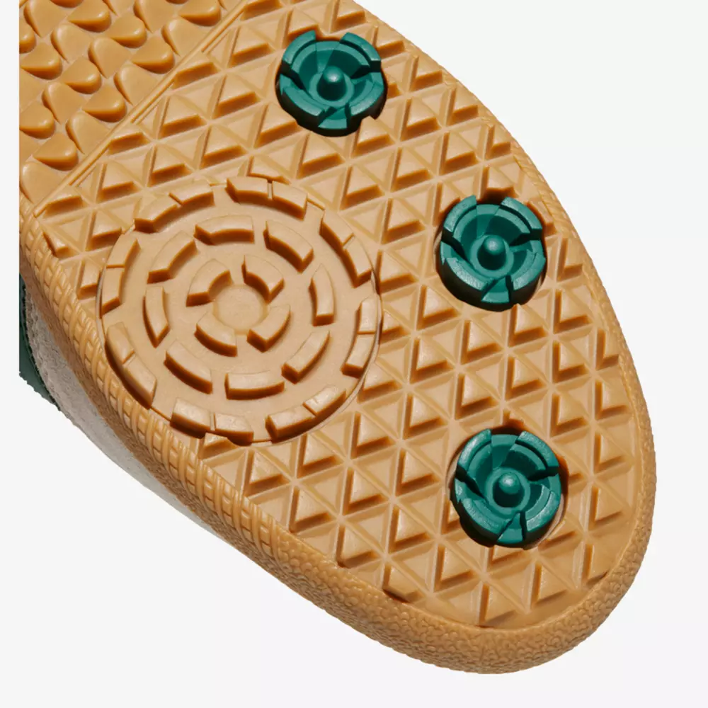 Close-up of a shoe sole from one of the best women's golf shoes 2026, featuring a tan, textured, triangular tread pattern with four green circular cleats&mdash;three at the front and one toward the back.