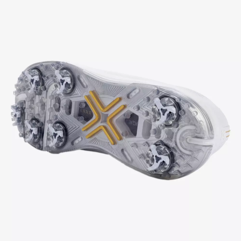 The image shows the underside of a white athletic shoe with a transparent sole, featuring six metal cleats and a yellow X-shaped support structure&mdash;elements often found in the best Jordan golf shoes.