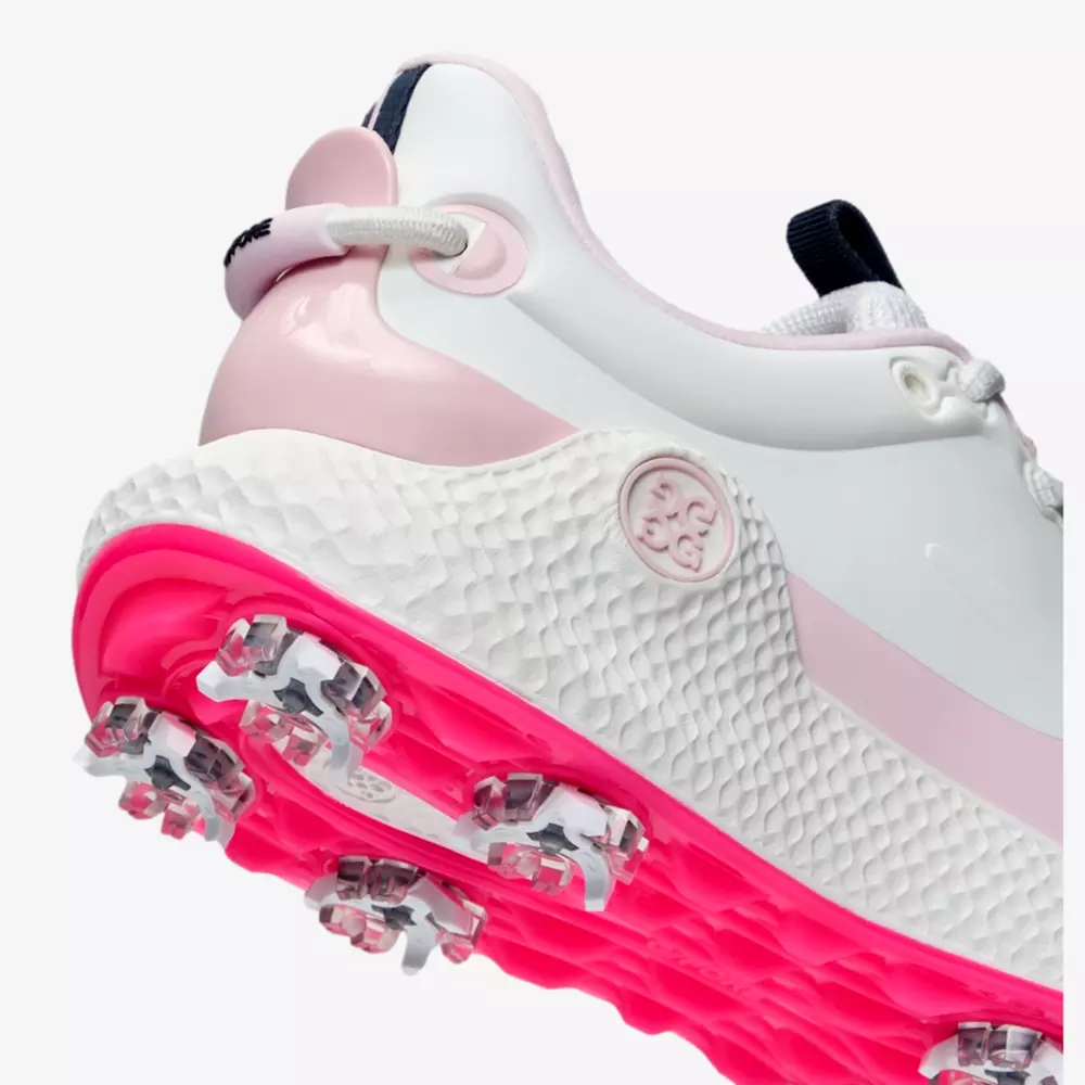 Close-up of a white and light pink athletic shoe with textured white midsole, hot pink outsole, and multiple metal spikes&mdash;one of the best golf shoes 2026, designed for top performance on the course.