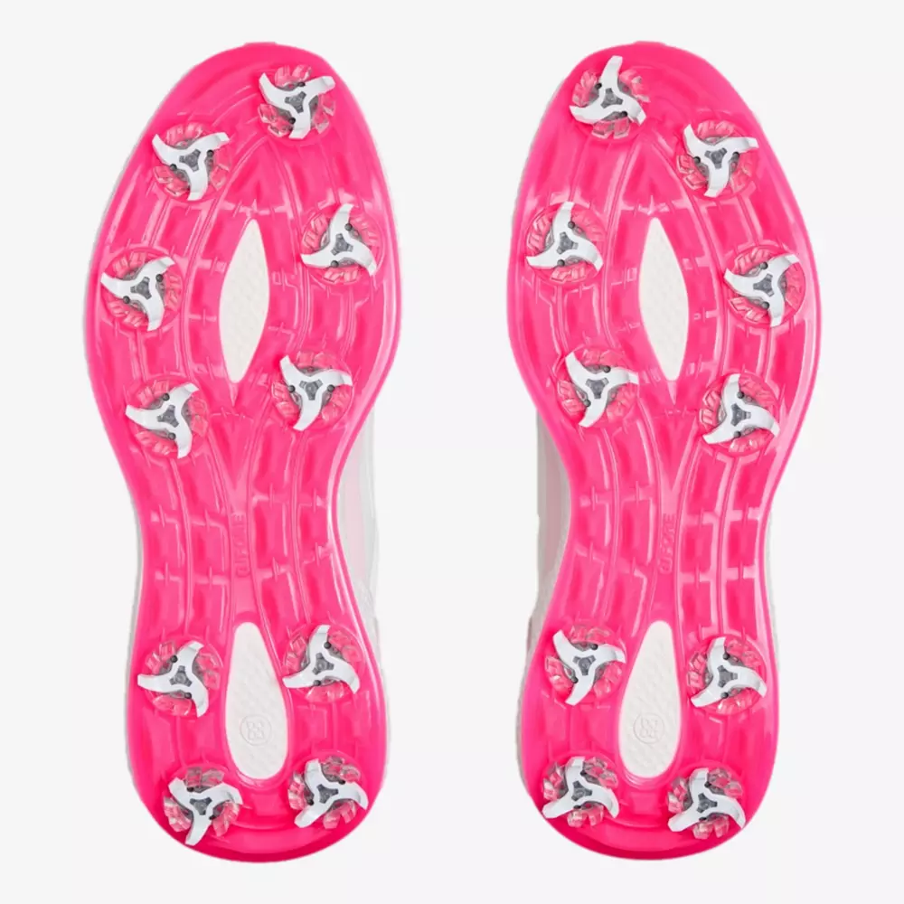A pair of soccer cleats shown from the bottom, featuring bright pink soles with multiple silver studs arranged for traction&mdash;offering innovative grip much like the best golf shoes 2026.