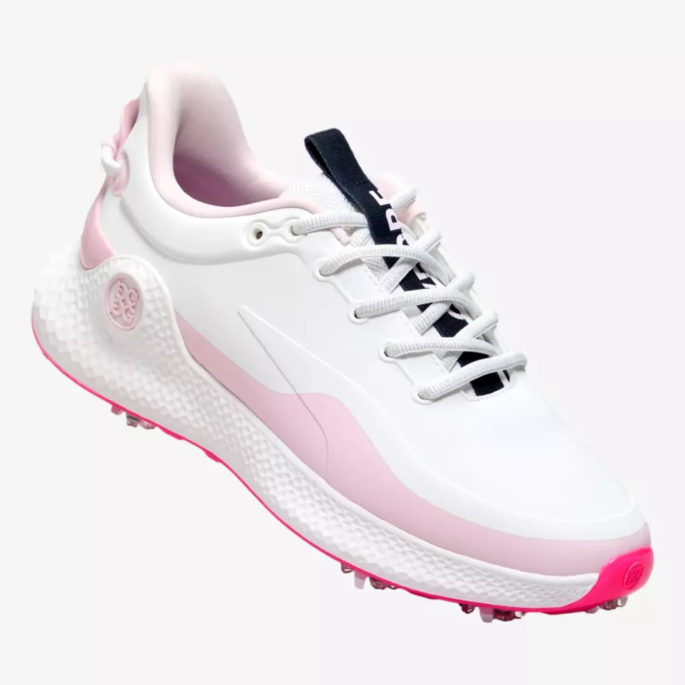 A white athletic sneaker with light pink accents, a textured sole, and a black tongue featuring white text. The modern design and grip studs on the pink outsole make it a standout among the best golf shoes 2026 has to offer.