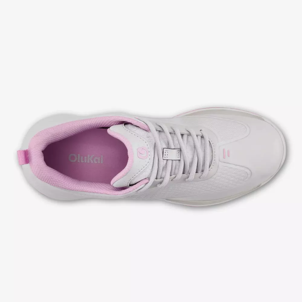 Top view of a white athletic sneaker with light pink interior lining, pink pull tab at the heel, and OluKai branding on the insole&mdash;an ideal pick for those seeking the best golf shoes 2026. The shoe features white laces and a modern, sleek design.