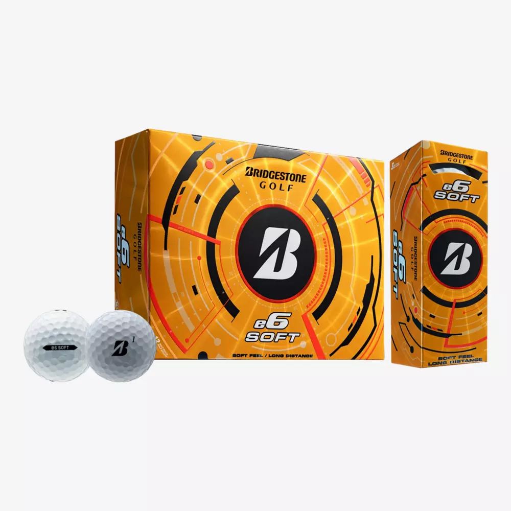 Two white Bridgestone golf balls sit before orange e6 Soft boxes, displaying a bold B logo with circular, tech-inspired graphics&mdash;perfect to pair with the best golf shoes 2026 has to offer for your next round.
