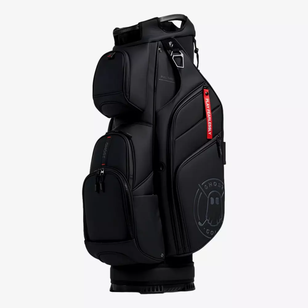 A black golf bag with multiple zippered compartments, a handle on top, a red tag reading FRAGMENT, and a subtle ghost logo on the lower side&mdash;an eye-catching contender for the best golf bags 2026. The bag stands upright against a plain white background.