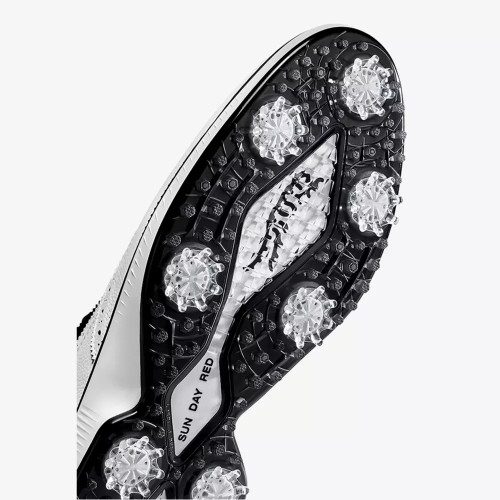 Close-up of the black and white sole of a golf shoe, featuring multiple clear, spiked cleats and textured grip patterns. The brand name &ldquo;FootJoy&rdquo; and &ldquo;SUNDAY RED&rdquo; are visible, reminiscent of the best Jordan golf shoes in style and performance.