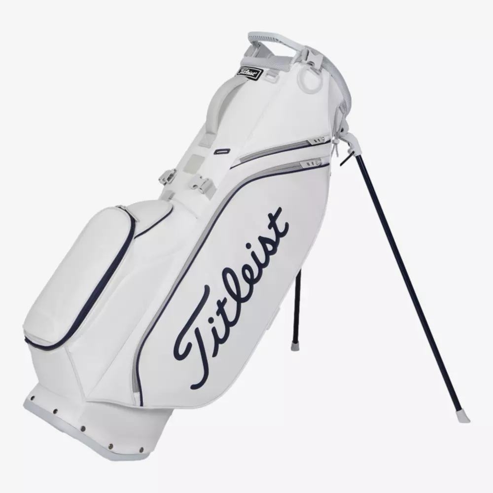 A white Titleist golf bag with navy blue accents and logo, featuring a stand and multiple zippered compartments, stands upright on its extended legs&mdash;a sleek contender among the best golf bags 2026.