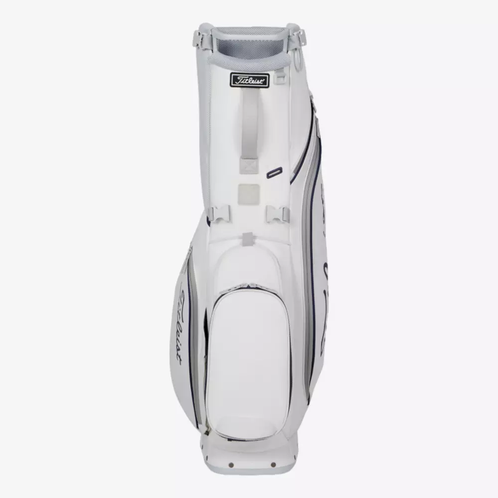 A white Titleist golf bag with multiple zippered compartments and handles, standing upright on a plain light background. The Titleist logo is visible on the side and near the top&mdash;an excellent choice among the best golf bags 2026.