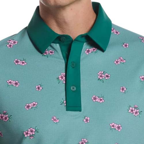 Close-up of a person wearing a teal polo shirt with a dark green collar and pink floral print, capturing one of the best looks from The First Major. The image focuses on the shirt from shoulders to upper chest; the face remains unseen.