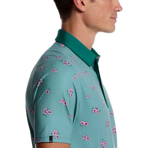 A man wearing a teal polo shirt with a dark green collar and a pattern of small pink flowers, shown from the side facing right—one of the best looks from The First Major.