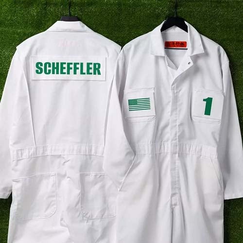 Two white coveralls on hangers against green grass. One displays SCHEFFLER in green letters on the back; the other highlights a green U.S. flag and the number 1 on the front—perfect alongside your best Jordan golf shoes.
