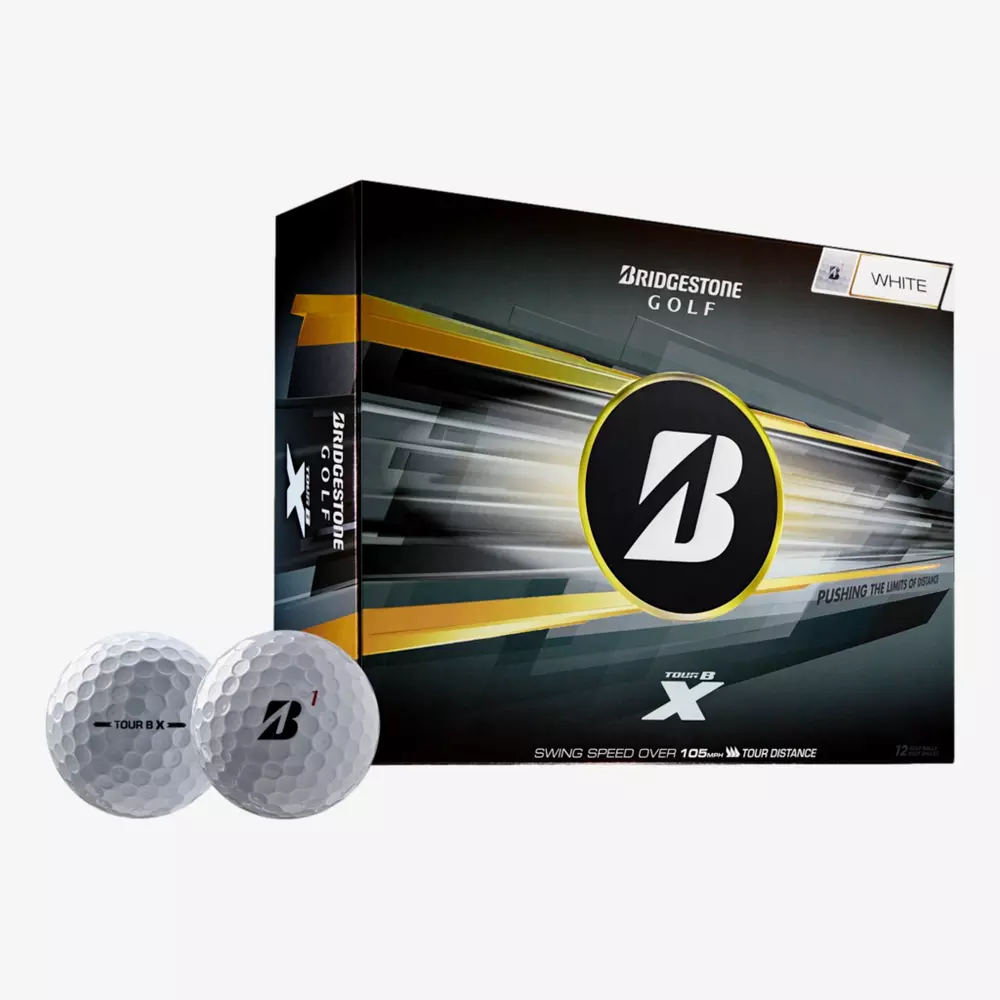 A box of Bridgestone Golf Tour B X white golf balls is shown, with two golf balls placed in front. The black, yellow, and silver packaging featuring the Bridgestone logo sits beside a pair of the best golf shoes 2026.