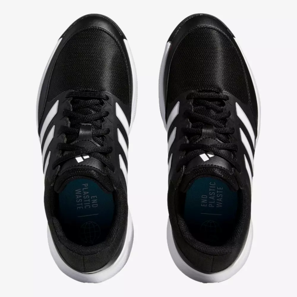 A pair of black athletic shoes with white soles and three white stripes on each side, viewed from above. The insoles display the text END PLASTIC WASTE and a globe icon&mdash;an inspired design for those seeking the best golf shoes 2026.