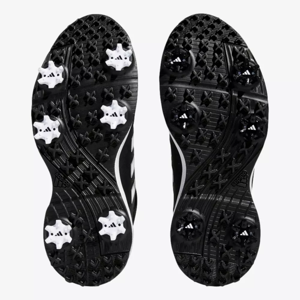 A pair of black sports shoe soles with multiple white and black cleats for traction, viewed from the bottom against a plain white background&mdash;perfect inspiration for the best golf shoes 2026.