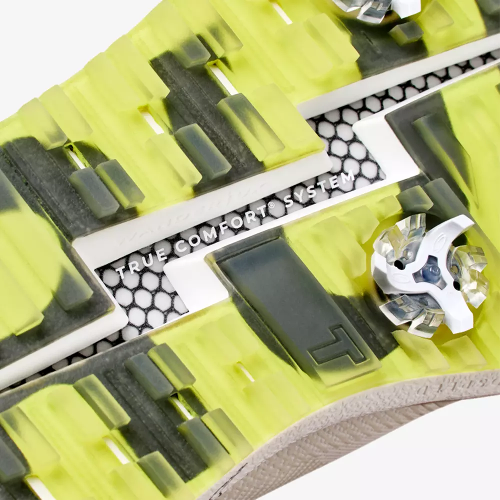 Close-up of a shoe sole with a bright yellow and gray tread, hexagonal black-and-white pattern, clear spikes, and the text TRUE COMFORT SYSTEM embossed in the center&mdash;reminiscent of the best Jordan golf shoes.