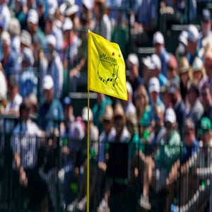 2026 Masters Saturday tee times: Yellow flag at Augusta National with fans in background.