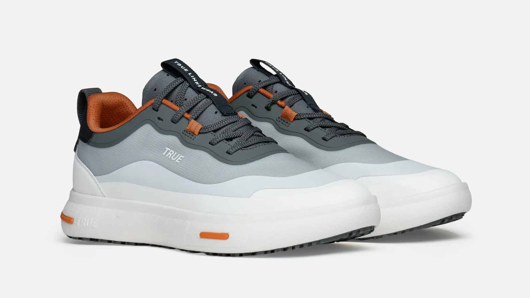A pair of modern, low-top True Linkswear golf shoes in shades of white, gray, and orange, featuring thick white soles, gray laces, and orange accents—perfect as comfortable golf shoes—placed on a plain white background.