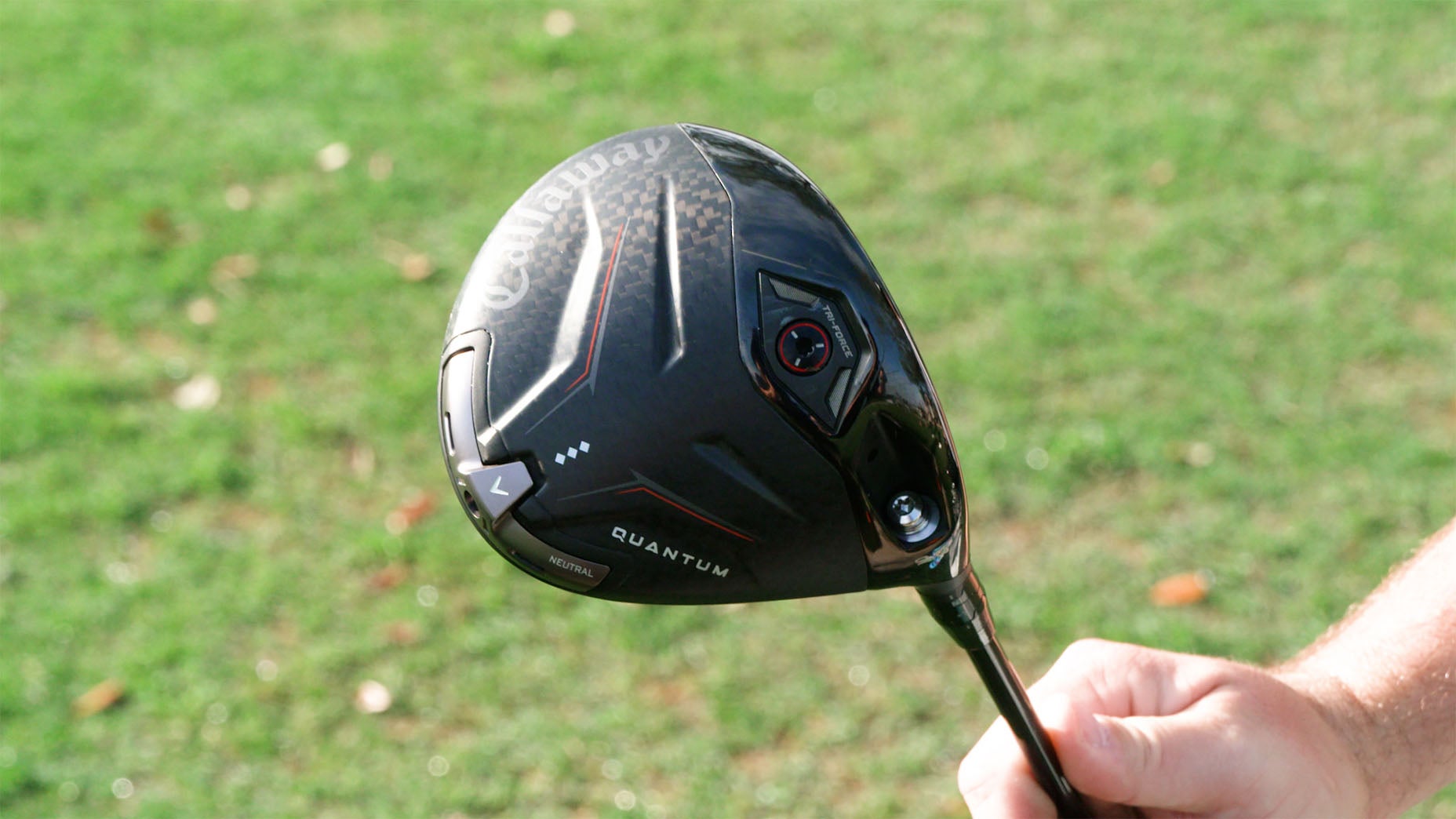 A person holds a black Callaway Quantum golf driver against a grassy background, with the clubheads branding and details clearly visible.