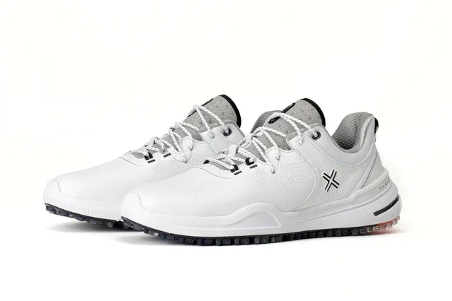 A pair of white athletic sneakers with gray accents, black treaded soles, and a black geometric logo on the side&mdash;styled to rival the best golf shoes 2026&mdash;displayed against a plain white background.