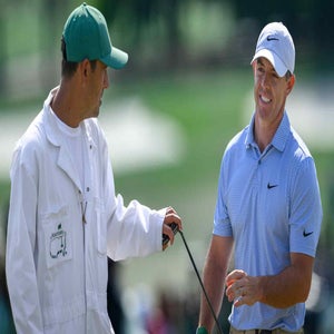 A golfer in a blue shirt and white cap smiles while talking to his caddie, both discussing their next move on the golf course during the Masters, where money and glory are on the line.