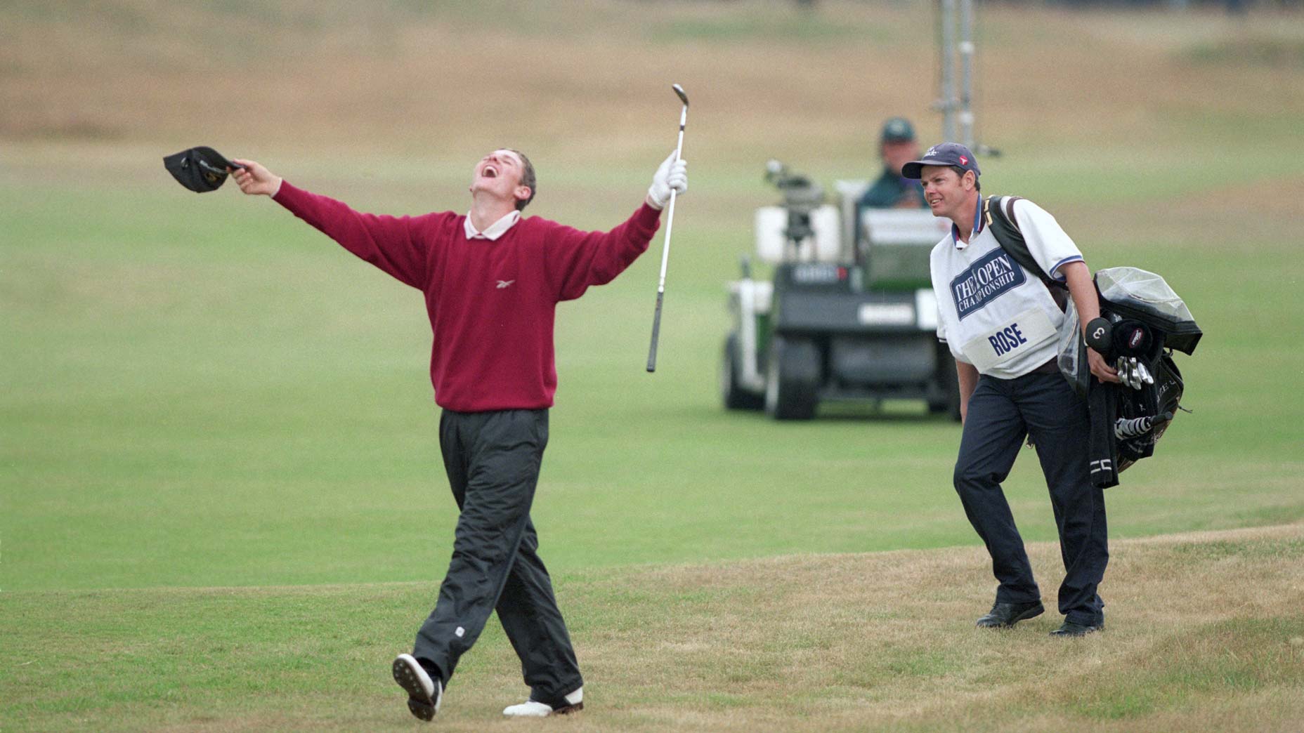 A golfer in a red sweater celebrates with arms raised and mouth open, holding a cap and club, echoing Justin Rose’s iconic moments, while a smiling caddie stands nearby on a golf course with green and brown grass.