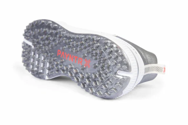 Close-up view of the sole of a sports shoe, positioned upside-down on a white background. Gray, multidirectional rubber studs and the word PAYNTR in red stand out&mdash;ideal for those seeking the best golf shoes 2026 has to offer.