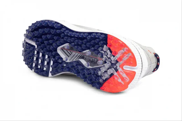 The image shows the sole of a sports shoe with blue and red textured rubber studs&mdash;ideal for those seeking the best golf shoes 2026. The word PAYNTR is printed in the center, surrounded by clear, blue, and red segments for superior grip.