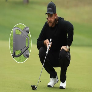 A golfer in black clothing and a cap crouches on the green, holding a putter. An inset shows a close-up view of the putter&rsquo;s head resting on the grass.