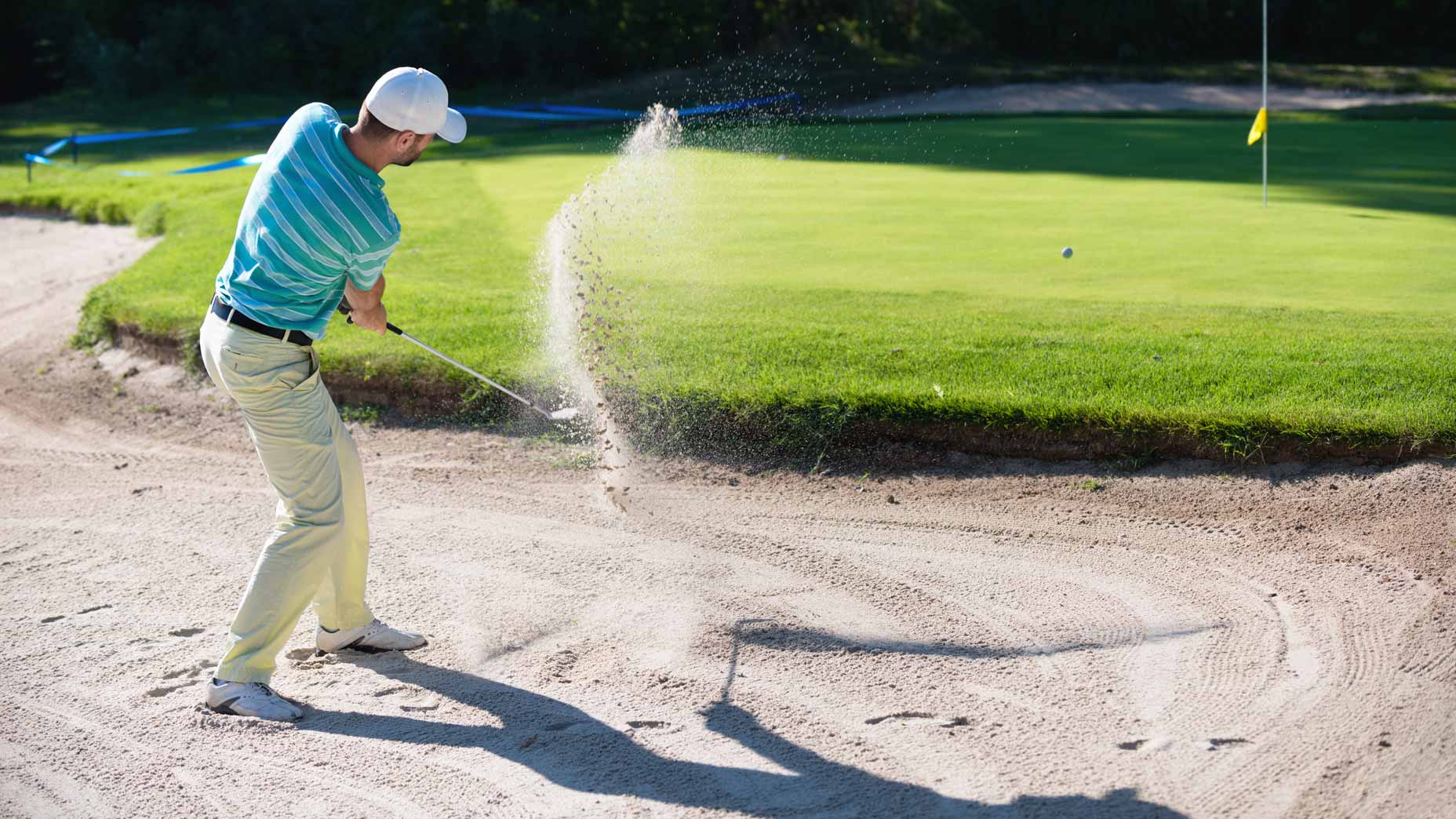 golfer in blue shirt hits bunker shot