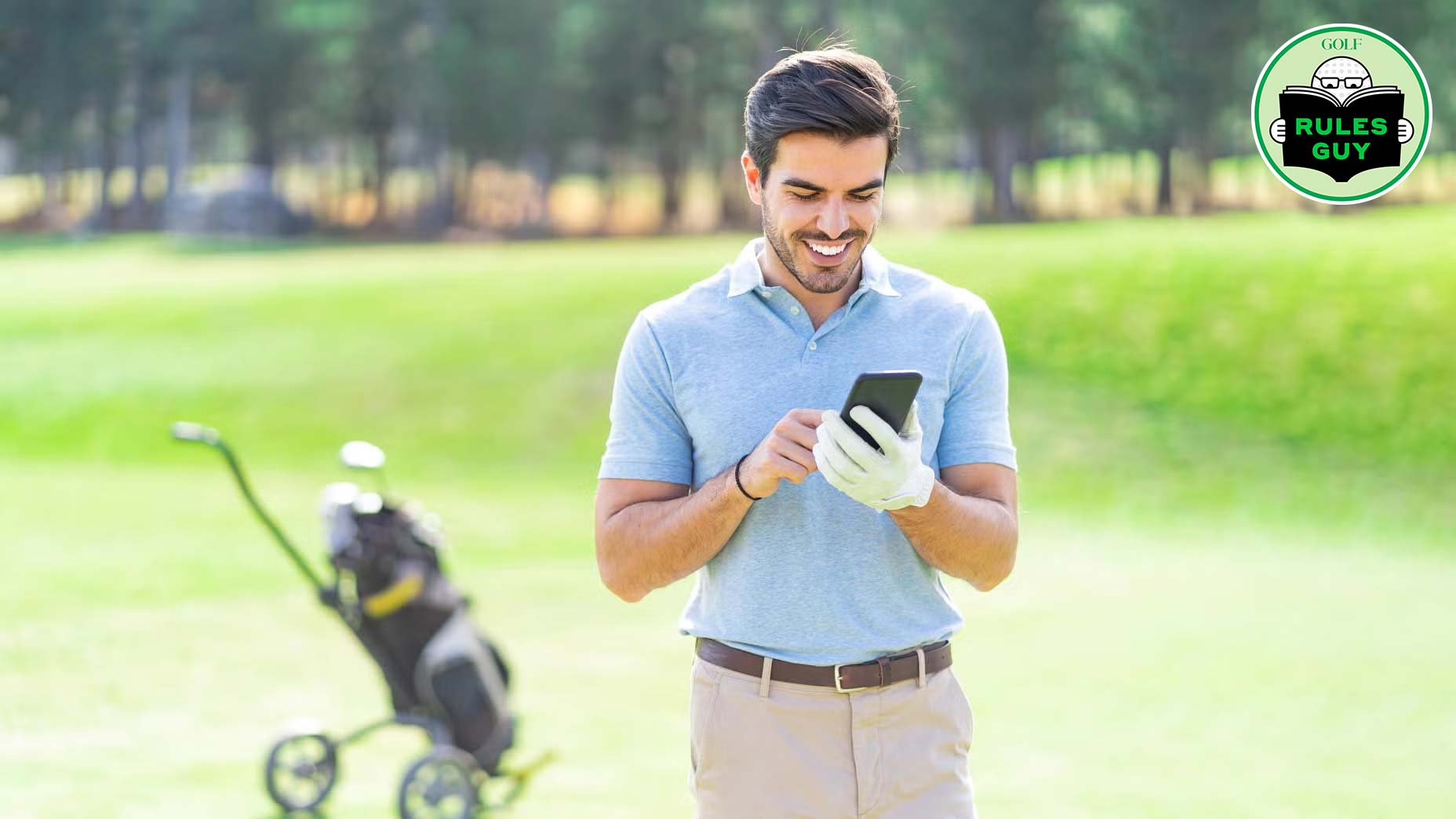 A man in a blue polo shirt and golf glove smiles while looking at his phone, possibly posting on social media, on a golf course. A golf bag on a pushcart is behind him, and trees are visible. A &ldquo;Rules Guy&rdquo; logo is in the top right corner.