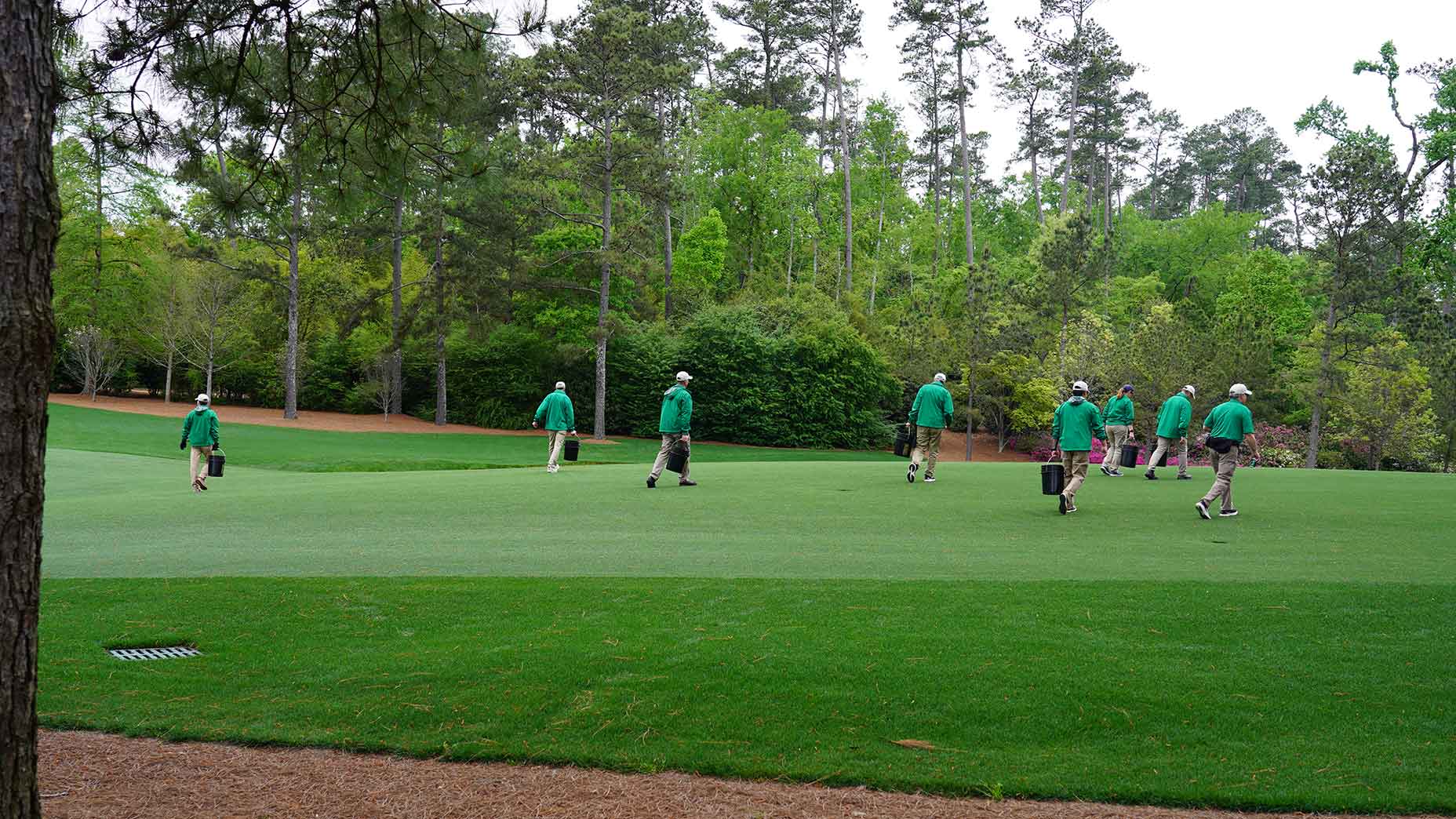A group of groundskeepers in green jackets and khaki pants walk across the 13th hole at Augusta National.