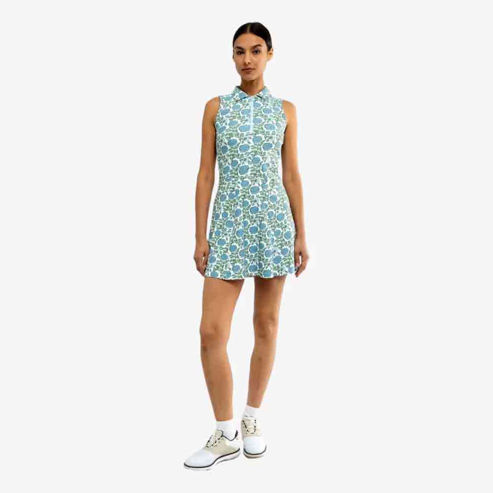 A woman stands against a plain background wearing a sleeveless blue and green dress with a floral print and white athletic shoes with ankle socks—a light and fresh look perfect for celebrating Mother's Day.