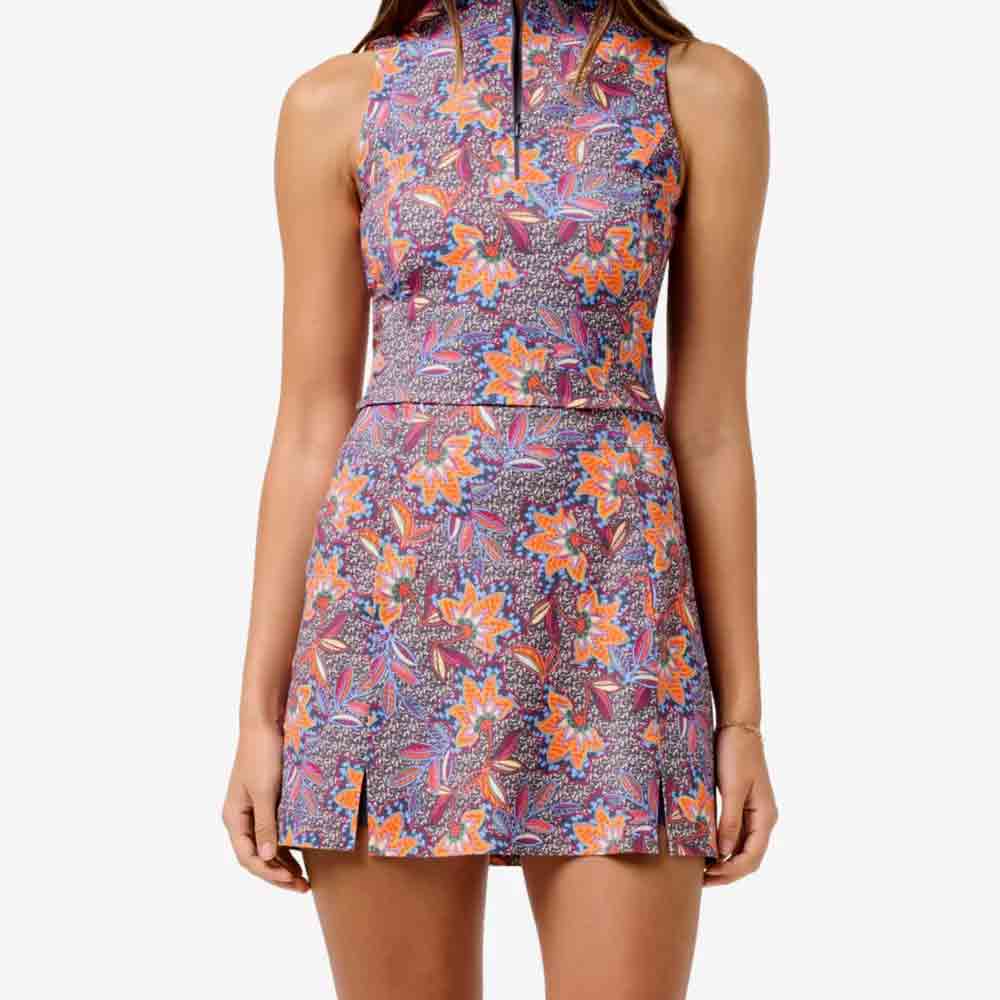 A woman wearing a sleeveless high-neck floral dress with a colorful pattern in purple, orange and pink - an elegant choice for Mother's Day. The dress features a fitted waist and short hem with small slits in the front.