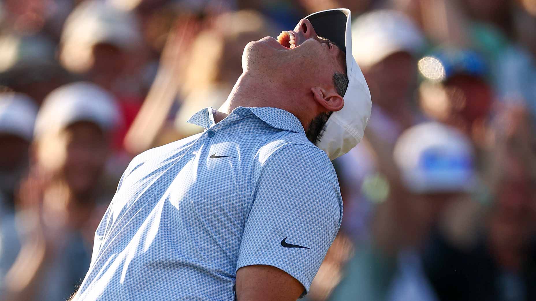A golfer wearing a white cap and light blue patterned shirt leans back, mouth open in celebration or relief at Augusta, with a blurred crowd cheering in the background—capturing the electric atmosphere of the Masters.