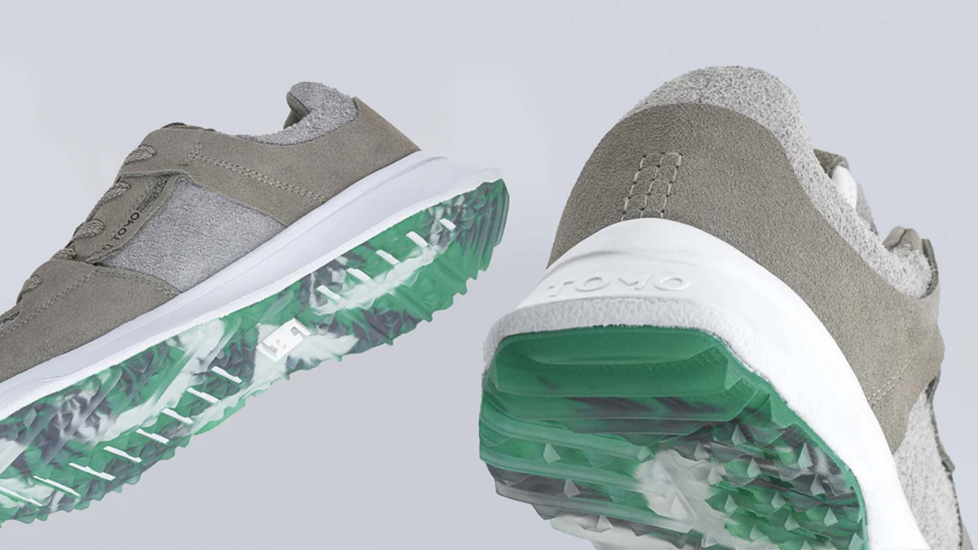Close-up view of two gray golf shoes featuring white midsoles and translucent green-and-white textured outsoles, set against a light gray background.