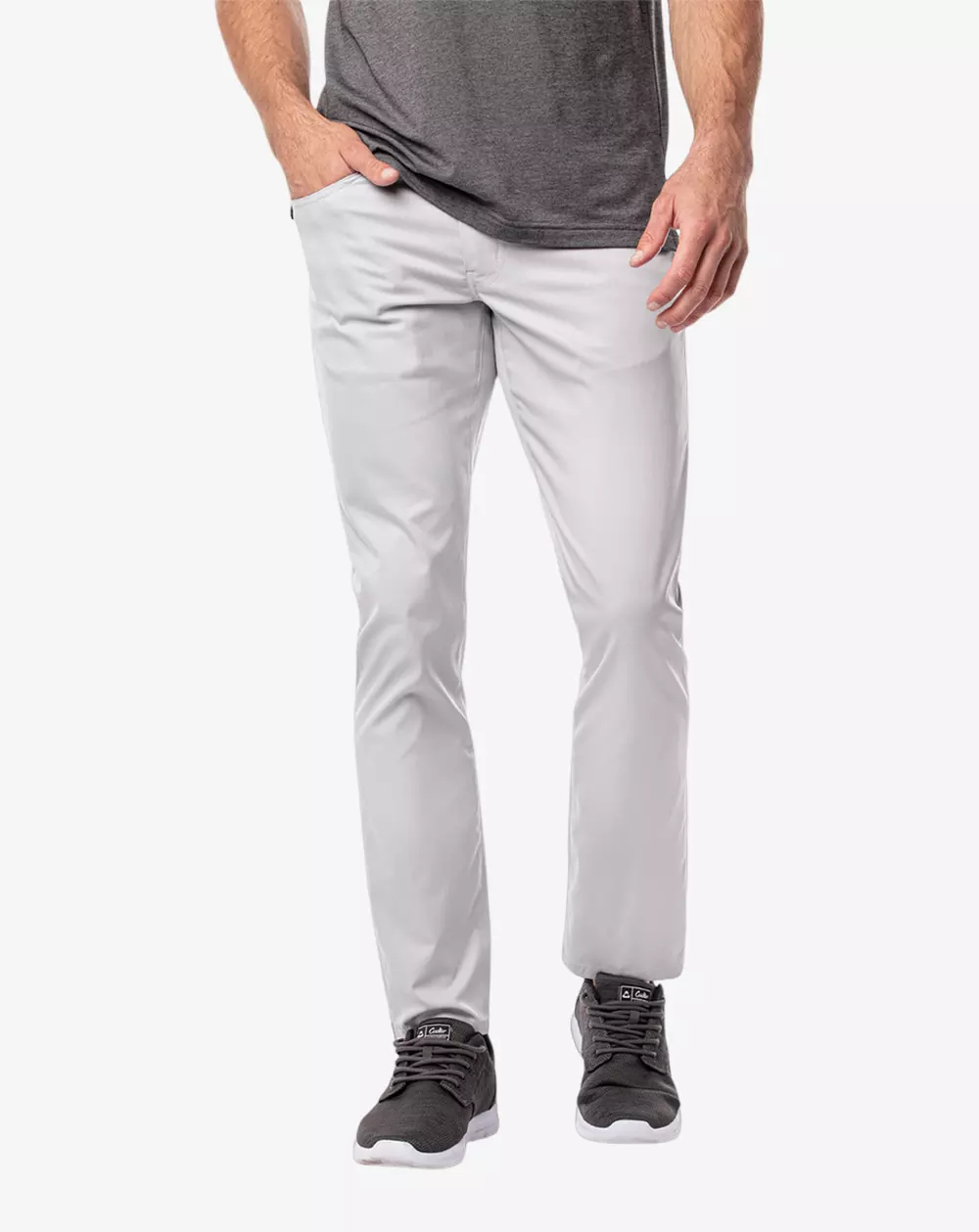 A person wearing light gray slim-fit pants, a dark gray t-shirt, and dark gray sneakers stands against a stark white background—perfect outfits for browsing the best golf travel bags. The human head is not visible in the picture.