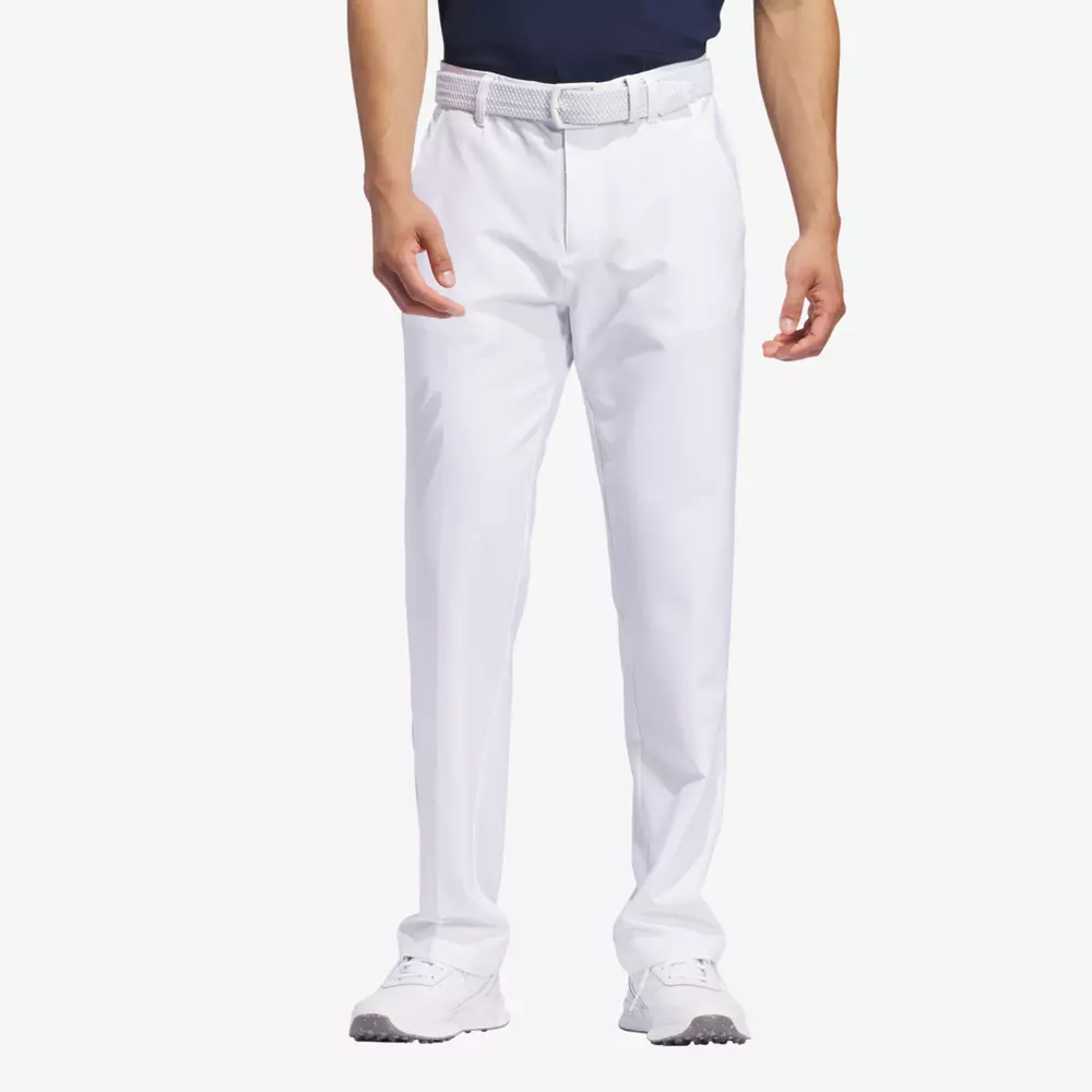 A man wearing white golf pants, a white belt, white golf shoes, and a black shirt stands with his hands relaxed at his sides against a stark white background—ready for the road or packing the best golf bags for his next trip.