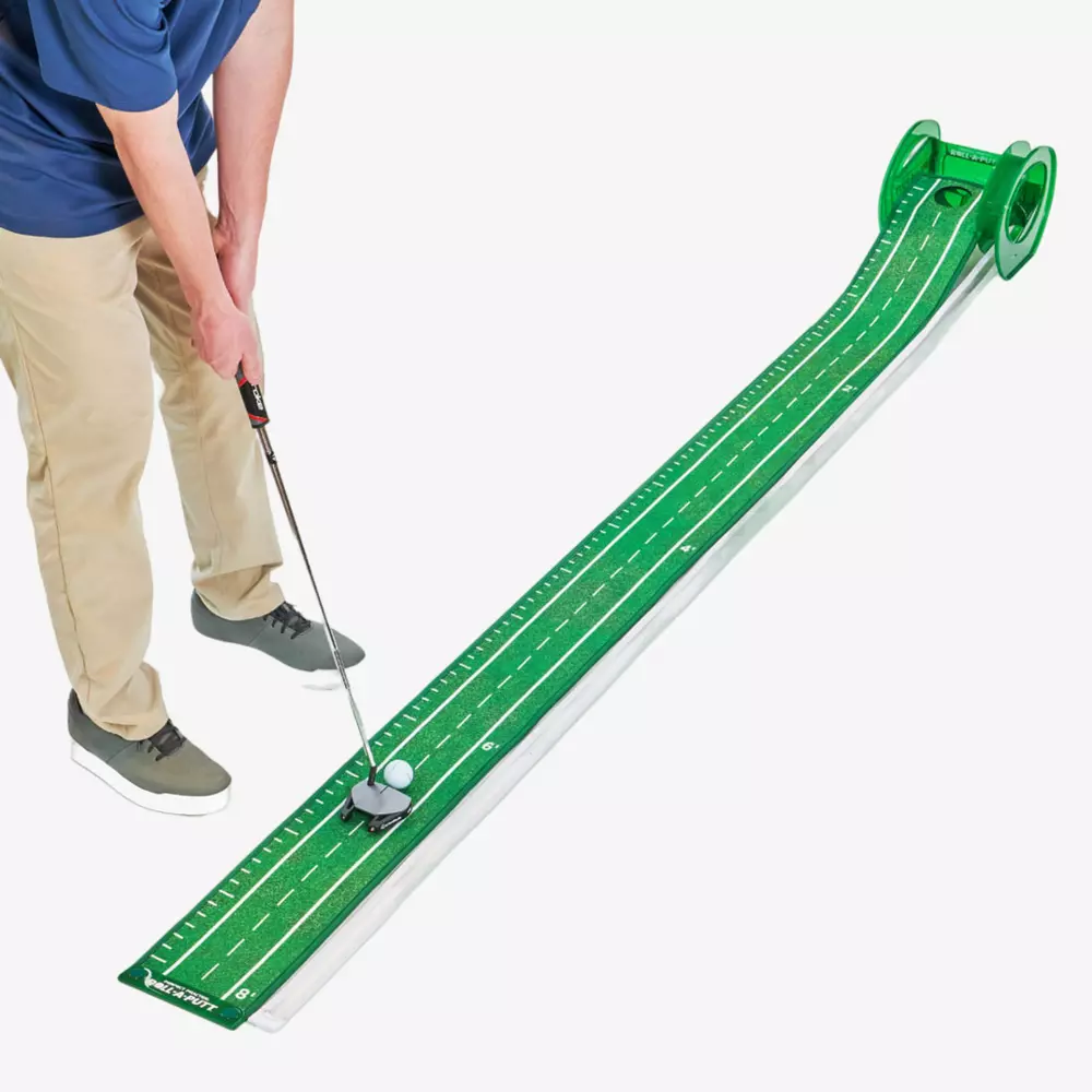 Person in khaki pants and gray shoes using a golf putter to hit a ball on a long, green indoor putting mat with white markings and a raised ball return system&mdash;one of the best deals under $50.
