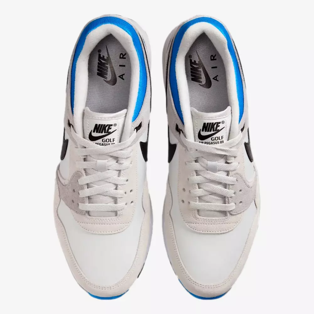 Top view of a pair of Nike Air Pegasus 89 golf shoes in white and light gray, blue inner lining, black swoosh, and Nike Golf Pegasus 89 text on the tongue—find the best deals under $50 on this stylish footwear.