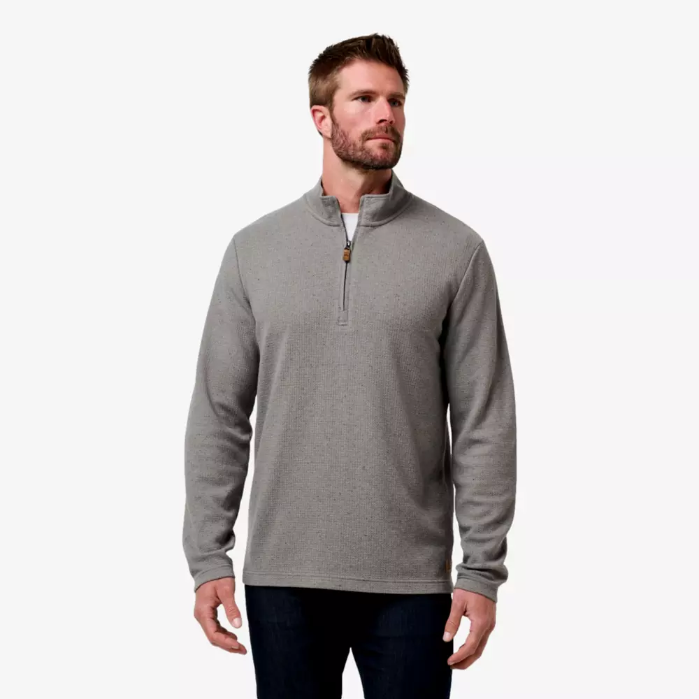 A man in a light gray quarter-zip pullover and black jeans—one of the best deals under $50—stands against a stark white background, looking slightly to the side with his hands loosely at his sides.