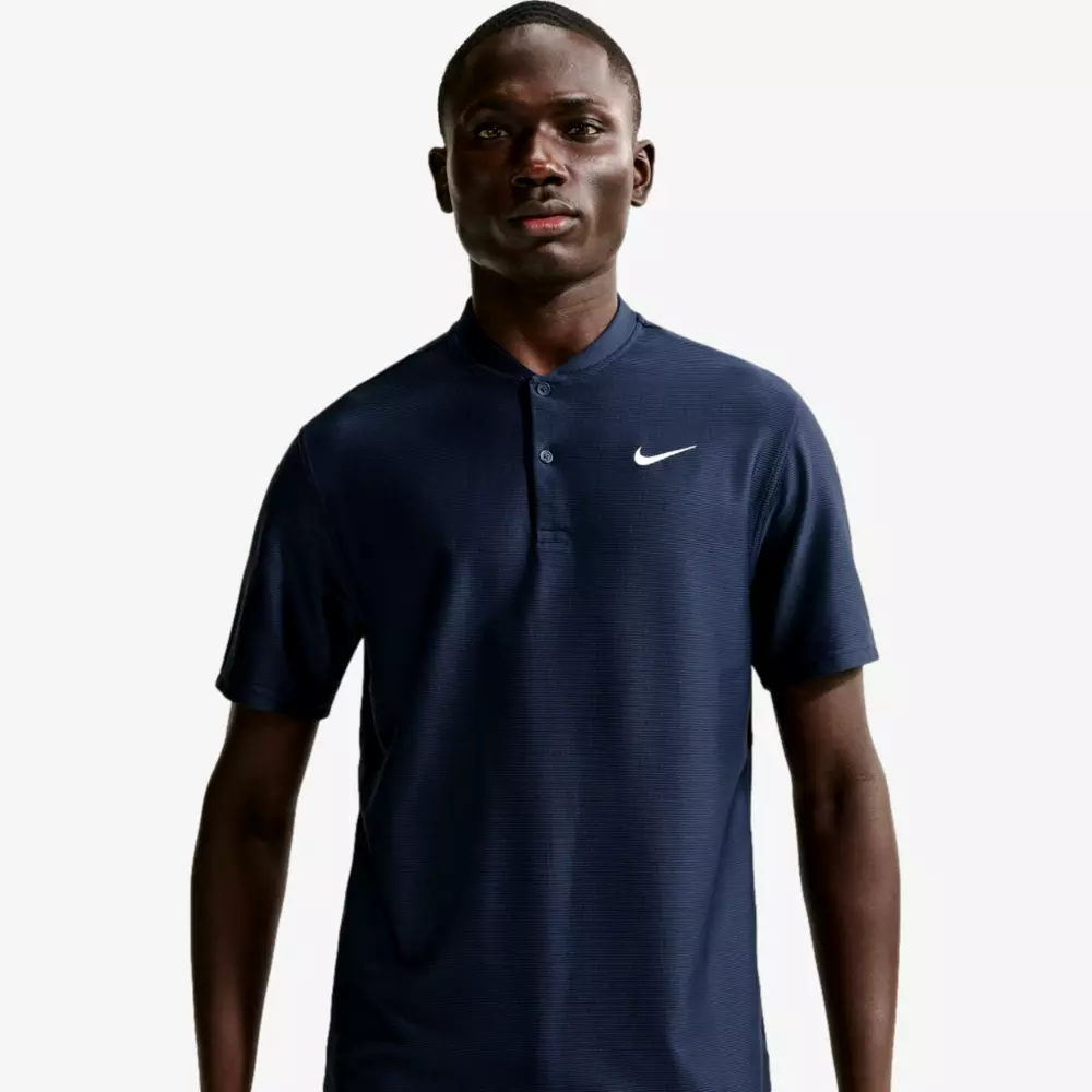 A man stands facing forward wearing a dark navy Nike polo shirt with a white Nike logo on the left chest, perfectly paired with the best golf pants. The background is plain and light-colored.