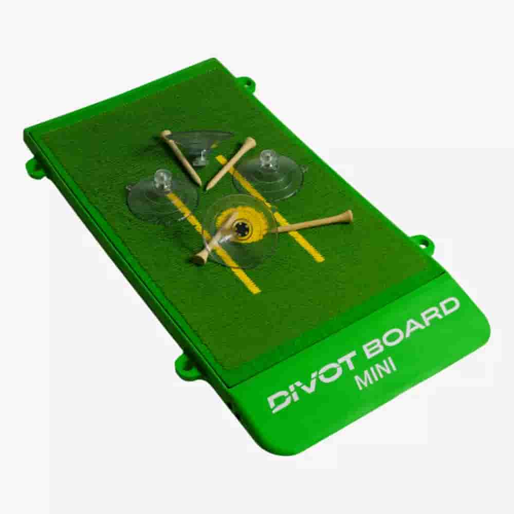 A green rectangular Divot Board Mini with artificial turf, yellow alignment lines, two suction cups, golf tees, and DIVOT BOARD MINI printed on the side—an ideal practice companion for those searching for the best golf bags 2026.