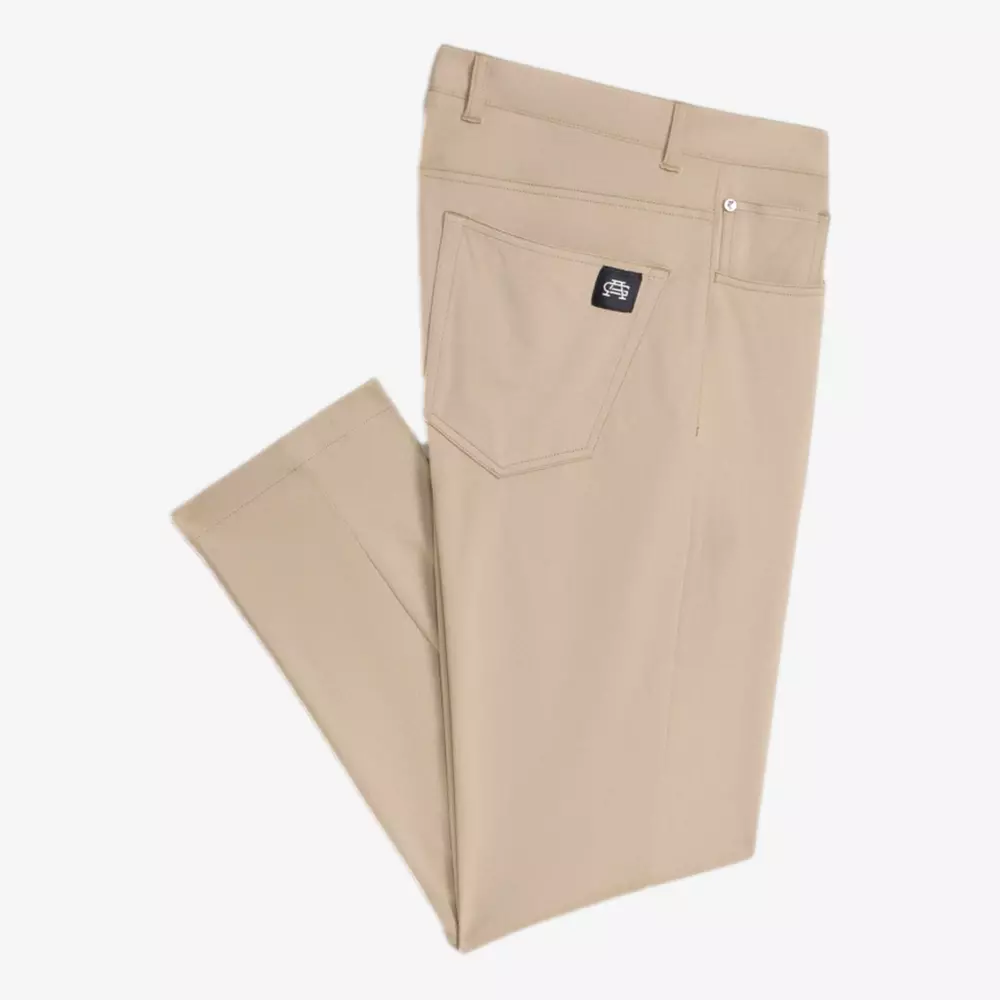 A pair of rolled-up beige pants with a back pocket featuring the brand's black stitched tag, laid flat on the white back—perfect for pairing with your go-to golf travel bags for your next getaway.