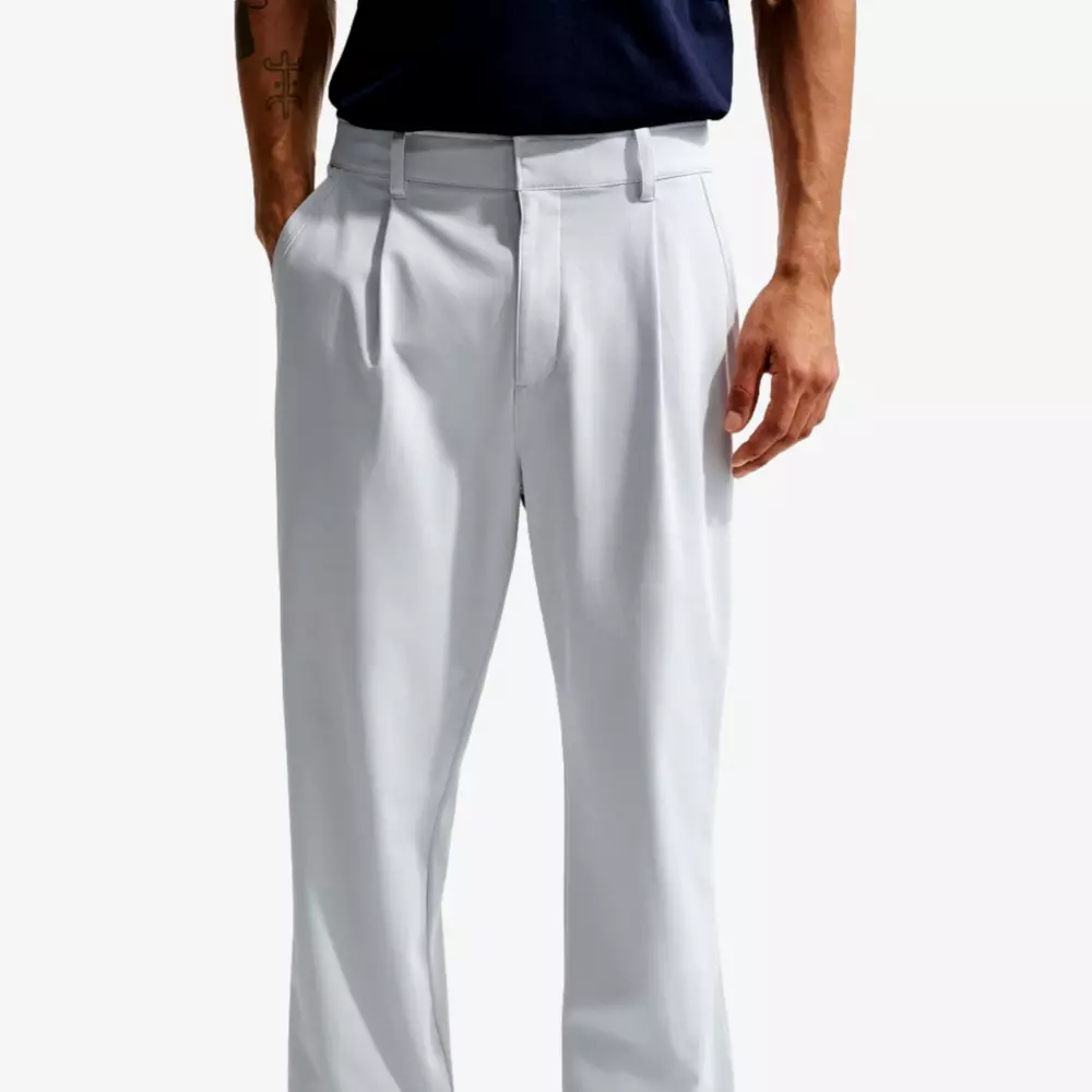A man wearing light gray button-down pants and a dark navy shirt, showing from the waist to mid-thigh, stands relaxed as if he's ready to pack for a trip with one of the best golf travel bags.