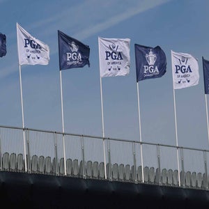 Several PGA of America and PGA Championship flags wave atop flagpoles on a structure against a clear blue sky, celebrating the spirit of the PGA Championship.