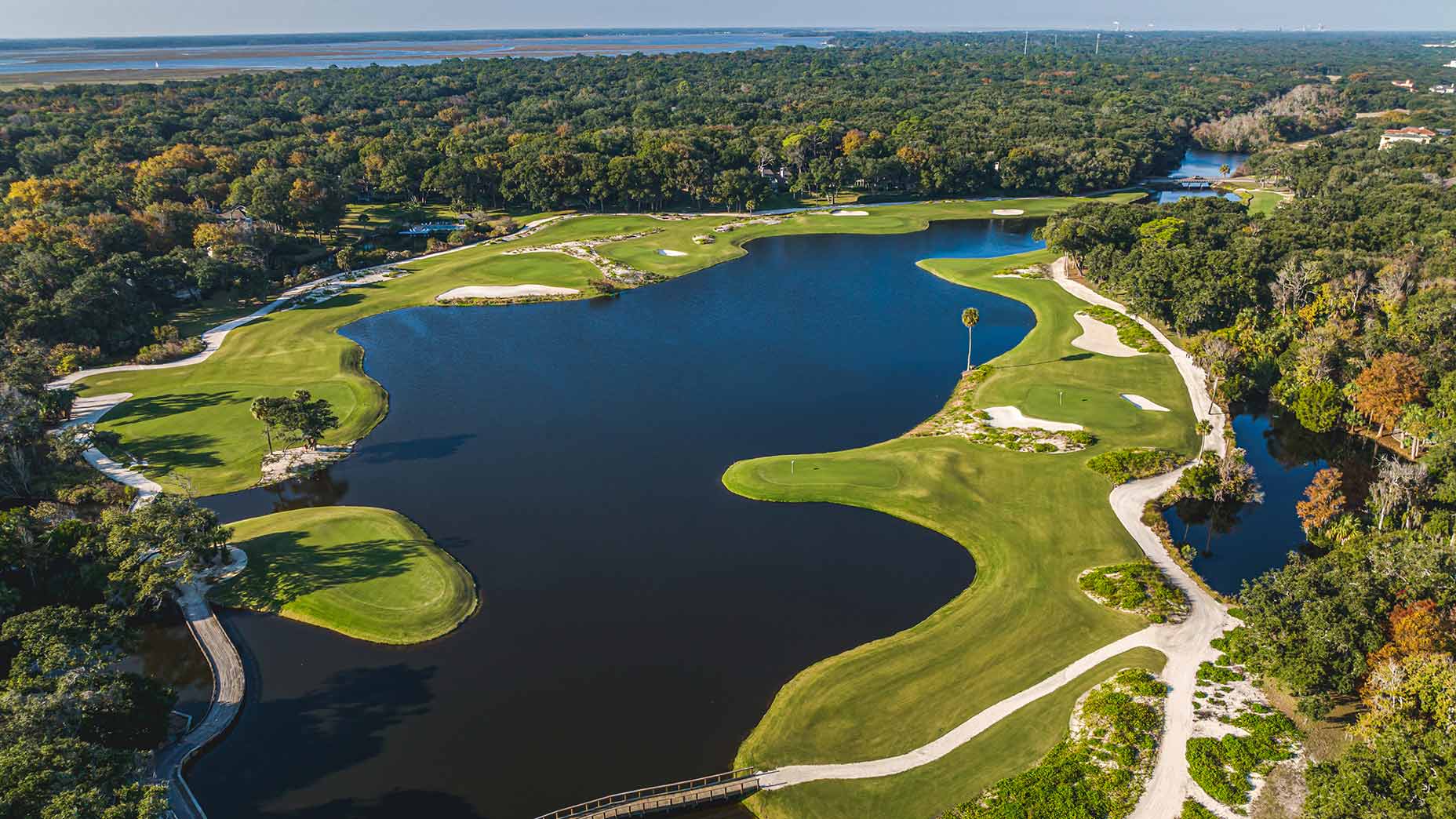 Aerial view of a lush golf course at Omni Amelia Island Resort with sand bunkers, winding fairways, and a central lake—perfect for a buddies' trip getaway—surrounded by dense trees under a clear sky.