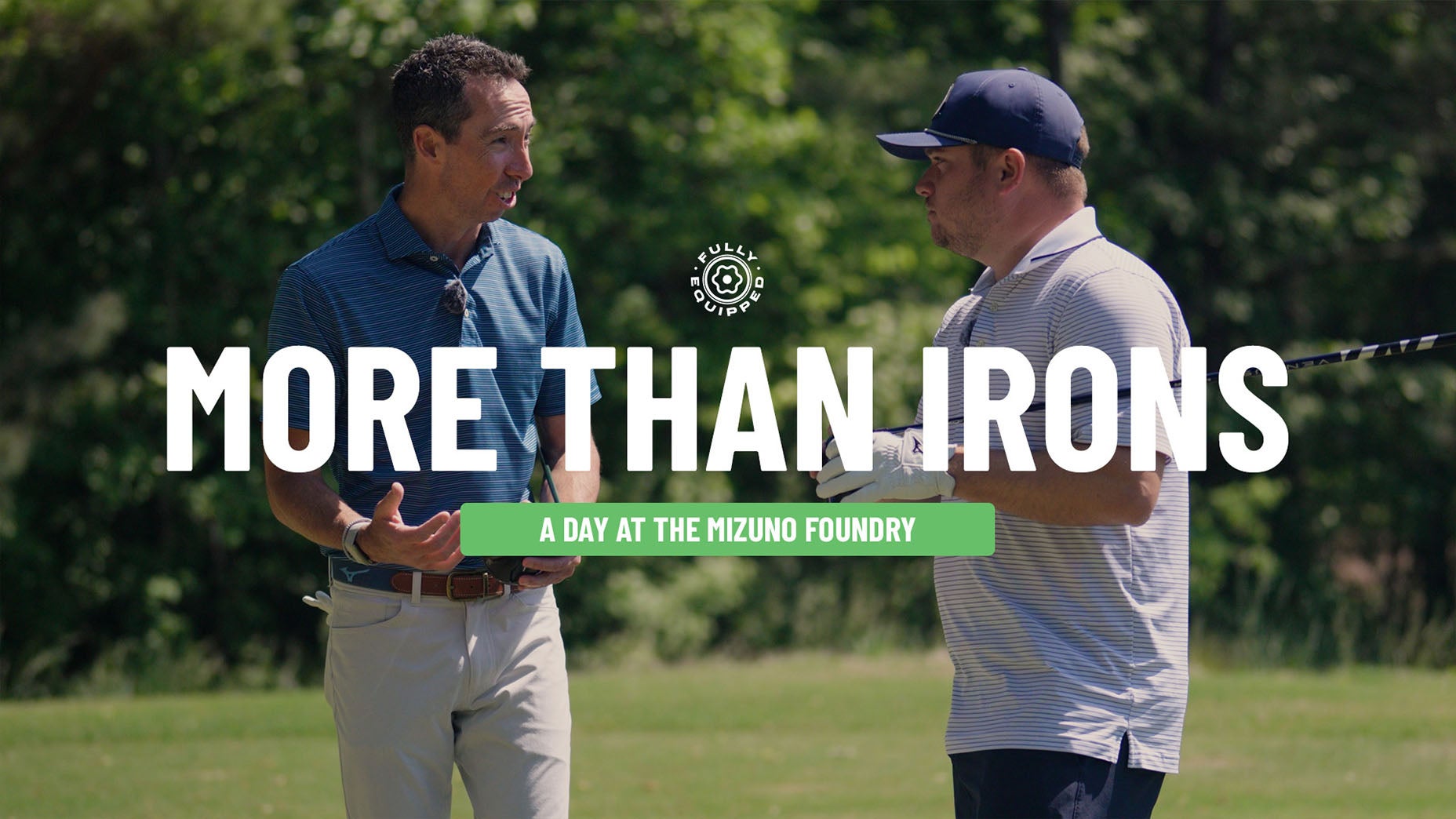 Two men stand outdoors on a golf course, talking. Both hold golf clubs—including the Mizuno JPX One Driver—and wear collared shirts. Text over the image reads, MORE THAN IRONS—A DAY AT THE MIZUNO FOUNDRY. Trees are visible in the background.