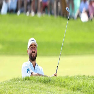 A golfer in a white cap and shirt hits a shot from a sand bunker onto the green at the CJ Cup Byron Nelson, with spectators watching in the blurred background&mdash;perfect action for fans seeking expert picks and tips.